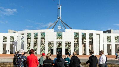 Tour group stands outside Parliament House on the Forecourt Mosaic listening to a tour guide