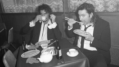 Peking Duk duo, Adam hyde having a sip of tea and Reuben Styles eating ramen at a restaurant.