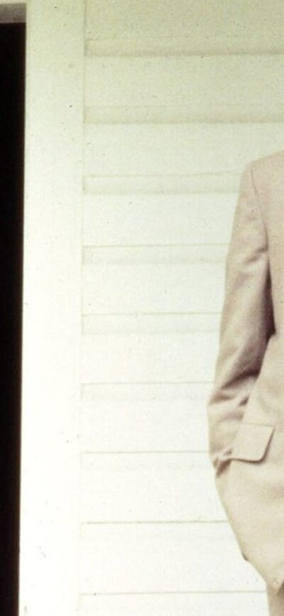 Witness (1958|M) Woman with bonnet stands to the right of man in tan coloured suit, both on a house porch