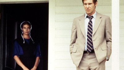 Woman with bonnet stands to the right of man in tan coloured suit, both on a house porch