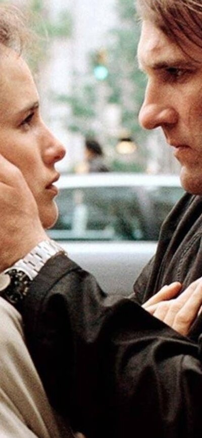 Green Card (1990 | M ) Woman with curly pulled back hair and man stand facing each other with his hands on her face