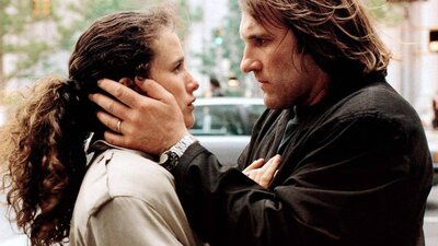 Woman with curly pulled back hair and man stand facing each other with his hands on her face