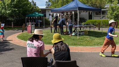 A photograph showing an outdoor scene of people outside tents on a sunny day