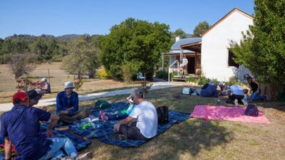 Group of people sitting on picnic blankets on grass next to a historic building.