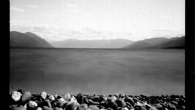 A black and white image of a rocky beach and water surrounded by mountains