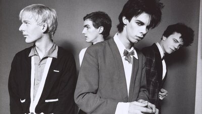A monochrome photographic portrait of four men with candid expressions wearing suits.