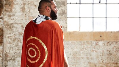 A man stand away from camera with a red cape and gold circles painted on it