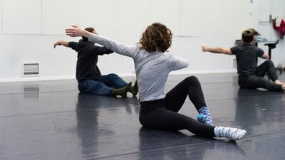 3 people are siting on the floor with thei legs outstretched. They are twisting away from the camera