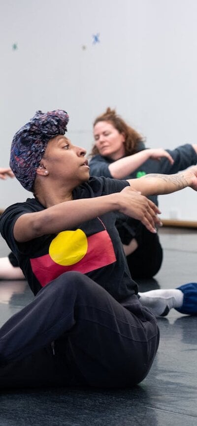 4 dancers are in the middle of twisting towards the camera. They are seated on the floor