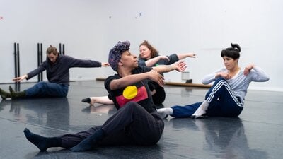 4 dancers are in the middle of twisting towards the camera. They are seated on the floor