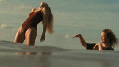Woman in bathing suit standing in water leaning back with another woman flicking water at her