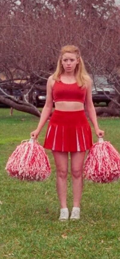 Cheerleader stands between white seating arrangement on green grass