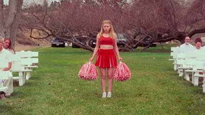 Cheerleader stands between white seating arrangement on green grass