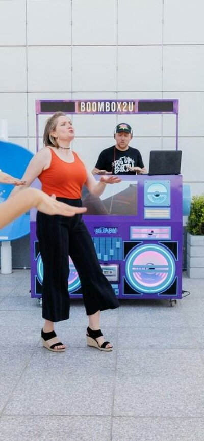 A group of people dancing in front of a DJ - Boom Box 2 U