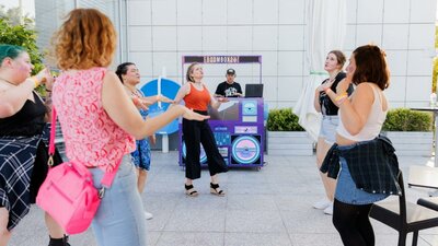 A group of people dancing in front of a DJ - Boom Box 2 U