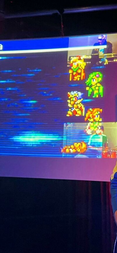 A man playing a guitar standing next to a TV screen with a video game