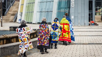 Canberra Quilters walking with colourful quilts over their shoulders through Civic Square