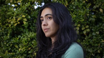 A young woman with long dark hair and a thoughtful expression looks off to the side., wearing green.