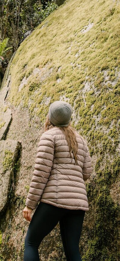 Woman hiking beside huge moss covered granite boulder