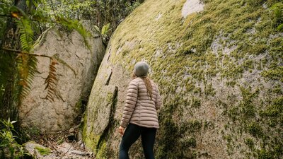 Woman hiking beside huge moss covered granite boulder