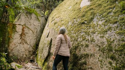 Woman hiking beside huge moss covered granite boulder
