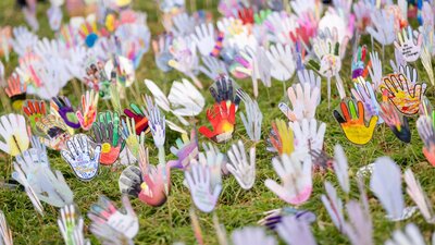 Colorful hand-shaped cutouts decorated with various patterns, mounted on sticks on grass area