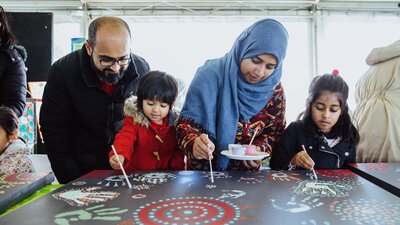 Family of four painting on large canvas decorated with colourful patterns and handprints