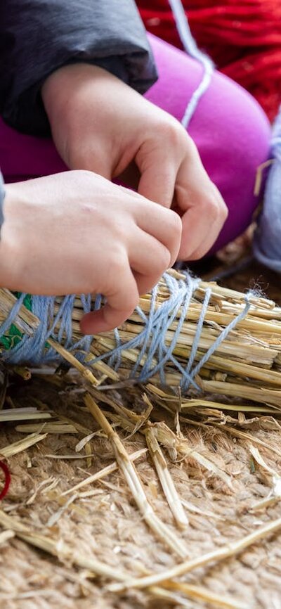 Person wrapping blue yarn around a bundle of straw