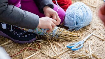 Person wrapping blue yarn around a bundle of straw