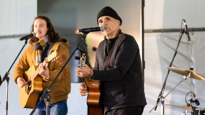 Two individuals playing acoustic guitars and singing into microphones on stage