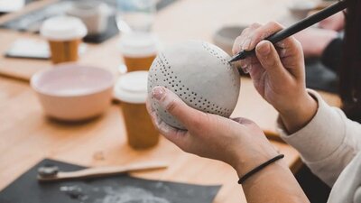Hands hold a clay sphere, poking holes in with a tool for decoration