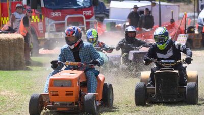 nla.obj-3640189333 Competitors race with lawnmowers on a grass track with a fire truck and spectators visible.