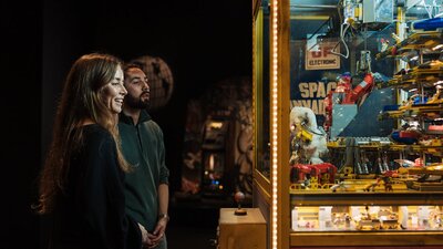 Adult couple enjoying observing a claw machine exhibit in RELICS