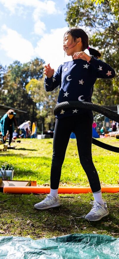 A young girl uses a bike tire as a hulla hoop in a park.