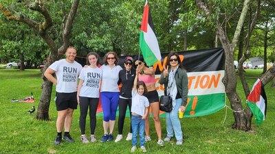 Runners (in run for Palestine T-shirts) and supporters with trees and Palestinian Flag in background