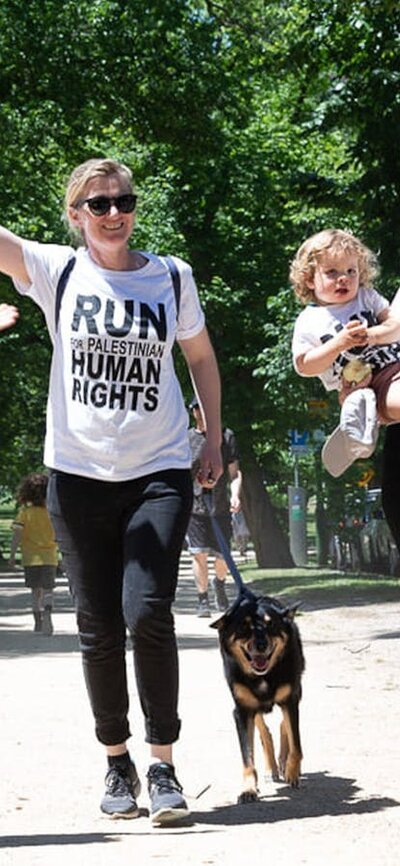 Three happy ladies, one with a child, one with a dog, all wearing run for palestine tshirts
