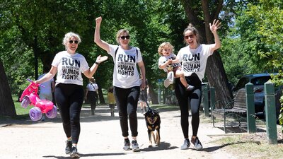 Three happy ladies, one with a child, one with a dog, all wearing run for palestine tshirts