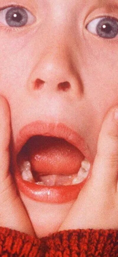Home Alone Young boy with mouth open holding his face in shock