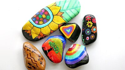 River rocks decorated in brightly coloured hand drawn images of flowers, trees, rainbows and pattern