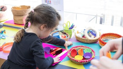 A young girl busy at a crafting table with colourful art supplies.