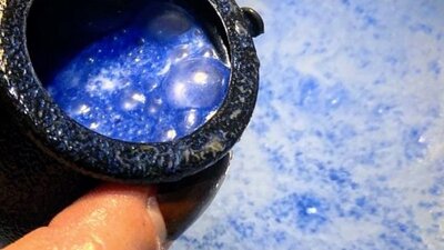 A bath bomb in cauldron, fizzing blue in the bath