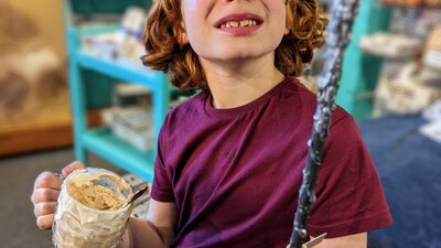 Photo of boy with a wand he made in a Quizzic Alley class and a QBrew in the other hand