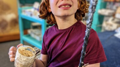 Photo of boy with a wand he made in a Quizzic Alley class and a QBrew in the other hand