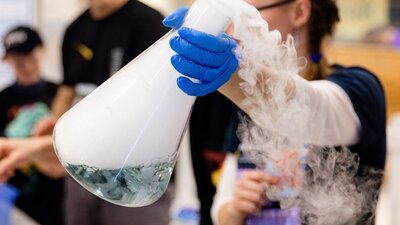 A person wearing a glove holding a large flask with dry ice steam coming out