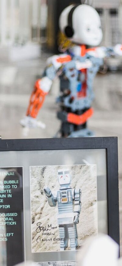An ipad in the foreground with 2 small humanoid robots in the background