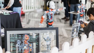 An ipad in the foreground with 2 small humanoid robots in the background