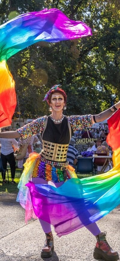 A drag king dances with rainbow fans and silks