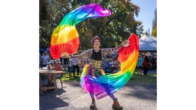 A drag king dances with rainbow fans and silks