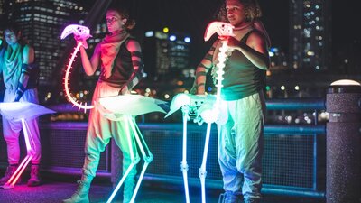 Two puppeteers operate rainbow LED flamingo skeletons