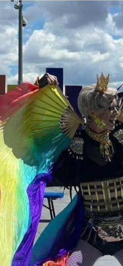 A drag king dances with rainbow fans and silks